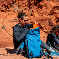 Person packing a blue GORUCK backpack on red rock outdoors, rucking gear adventure