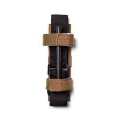 A Tourniquet Attachment in black, fastened with two tan hook-and-loop retention straps, is photographed on a white background from a top view.