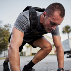 A man in workout gear leans forward, sweating and exhausted, during outdoor exercise while wearing the Training Weight Vest 2.0.