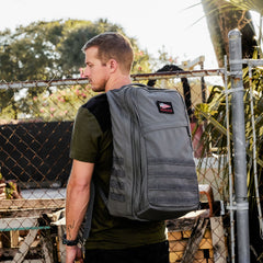 A man in a green shirt stands outside by a fence, wearing the large gray GR2 USA - Cordura backpack.
