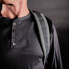A person wears the GR2 USA - Cordura, a black travel backpack with carry-on compliant design and sturdy strap, slung over their shoulder against a dark background.