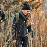Woman wearing black GORUCK vest and beanie, hiking outdoors with backpack in tall grass