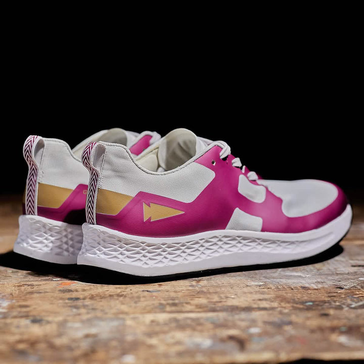 The Men's Rough Runner - Baton Rouge by GORUCK, featuring a contemporary design with pink and white panels and a geometric pattern on a textured sole, are stylishly displayed on a rustic wooden surface against a dark background, perfectly capturing the essence of the Rough Runner spirit.