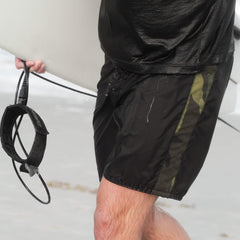 Close-up of a man in wet black and camouflage swim shorts holding a surfboard leash on the beach