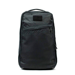 The GR1 USA - Heritage Waxed Canvas is a sleek black backpack featuring a front zipper pocket and top handle, displayed against a white background.