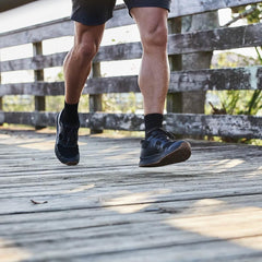 Close-up of muscular legs in shorts wearing black GORUCK shoes walking on wooden bridge outdoors