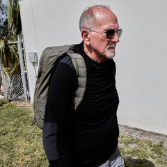 Man in sunglasses wearing a GORUCK backpack outdoors, dressed in black long sleeve shirt