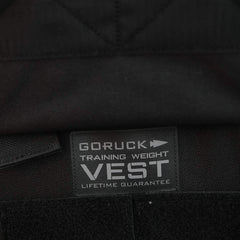 A close-up of a black fabric tag on a garment features the text "Training Weight Vest 2.0 LIFETIME GUARANTEE" above GORUCK's signature arrow logo, ideal for individuals looking for an adjustable weight vest experience.