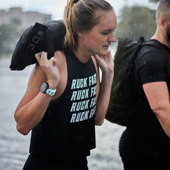 Woman in sleeveless 'Ruck Fast' shirt carrying 30-pound weight sandbag during outdoor rucking workout in rain