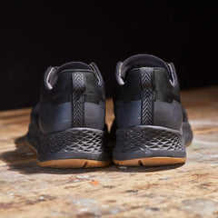 Pair of black durable rucking shoes with textured soles on a wooden surface against black background