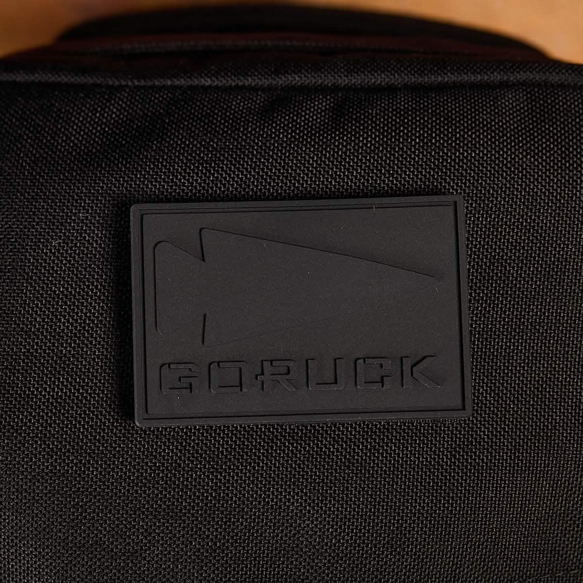 A detailed view of a PVC Patch from GORUCK, showcasing embossed text "GORUCK" accompanied by an arrow design. It is mounted on black material, possibly on a backpack or bag. This durable patch encapsulates the resilient and elegant spirit of Special Forces, reflecting the essence of the GORUCK spearhead.