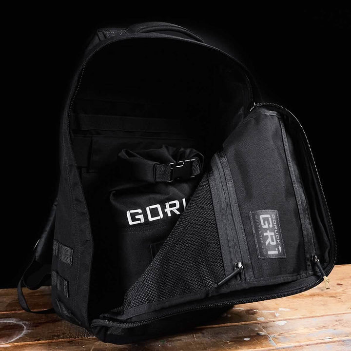 A GORUCK Brick Bag (5-50 LBS) with its main compartment open resembles military gear as it is packed and neatly placed on a wooden surface against a black background.