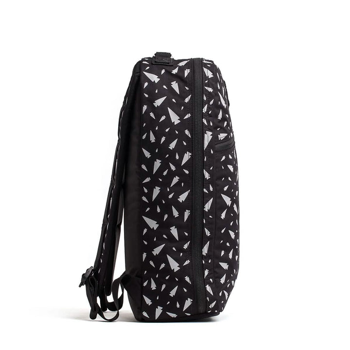 The Bullet Ruck - Classic - Reflective Spearhead by GORUCK is a 15L daypack made from durable Cordura fabric. It highlights a side view of its black design, adorned with a white geometric spearhead pattern. The pack includes a front zipper pocket and adjustable shoulder straps for comfort on the go.