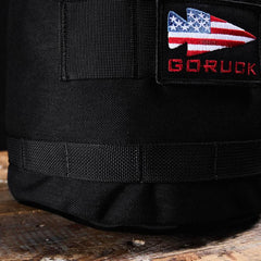 GORUCK black rucksack with American flag arrow patch on rugged wooden surface