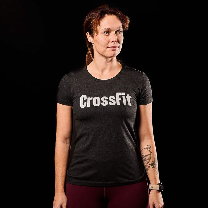 A person wearing a GORUCK Women's CrossFit Tee - Tri-Blend stands against a dark background.