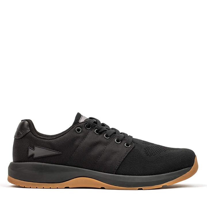 Introducing the Men's Ballistic Trainers from GORUCK in Black + Gum. These athletic workout shoes feature a textured design with six eyelets for laces and a contrasting tan sole. The distinctive black reflective spearhead logo adorns the side, and they are crafted with durable CORDURA® Ballistic Nylon. Set against a white background, these trainers are ideal for functional fitness enthusiasts.
