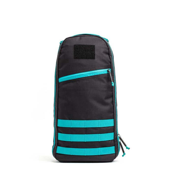 The GORUCK Bullet Ruck - 10L stands upright in a stylish black and teal design. Constructed with durable Cordura Fabric, it is equipped with a front zipper pocket, a top handle, and three horizontal teal straps near the base. Its sleek and modern design includes padded straps for added comfort.