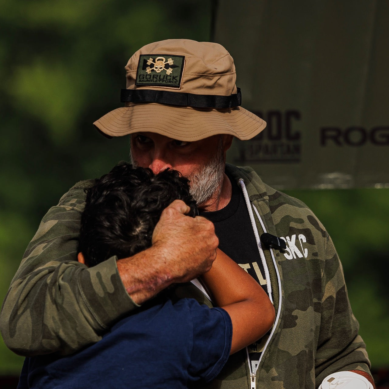 A man wearing a Boonie Hat - Tactical - ToughDry in camo hugs and comforts a child outdoors.