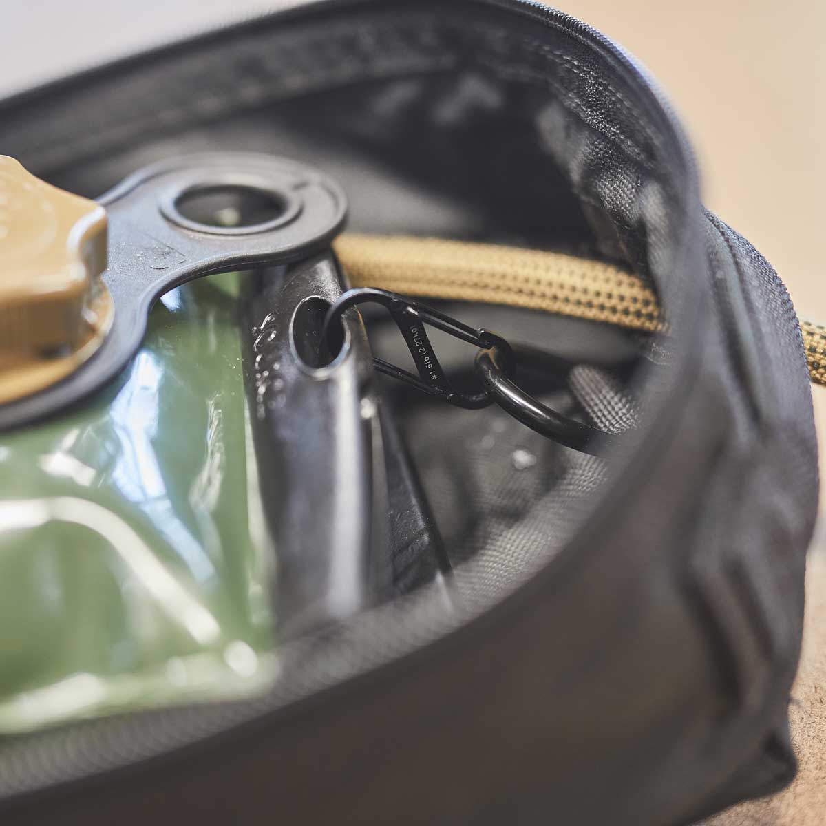 Close-up of a hydration bladder with a tan cap inside a black zippered bag, secured by a black carabiner.