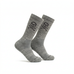 The Tribe Merino Challenge Socks - Crew are gray crew socks featuring a black skull and crossbones design on the side, shown against a white background.