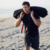 Man training on beach with GORUCK sandbag, wearing black athletic gear