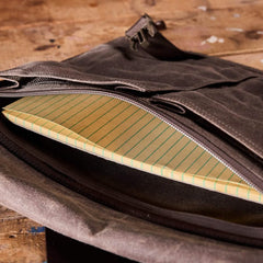 Open GORUCK's Heritage Claymore Sling Bag, made from brown waxed canvas, on a wooden surface, revealing a yellow legal pad with green lines partially zipped inside.