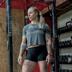 Athletic tattooed woman in gray crop top and black shorts training in gym with kettlebells and weight rack