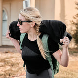 Woman rucking outdoors with GORUCK gear, wearing backpack and carrying weighted sandbag