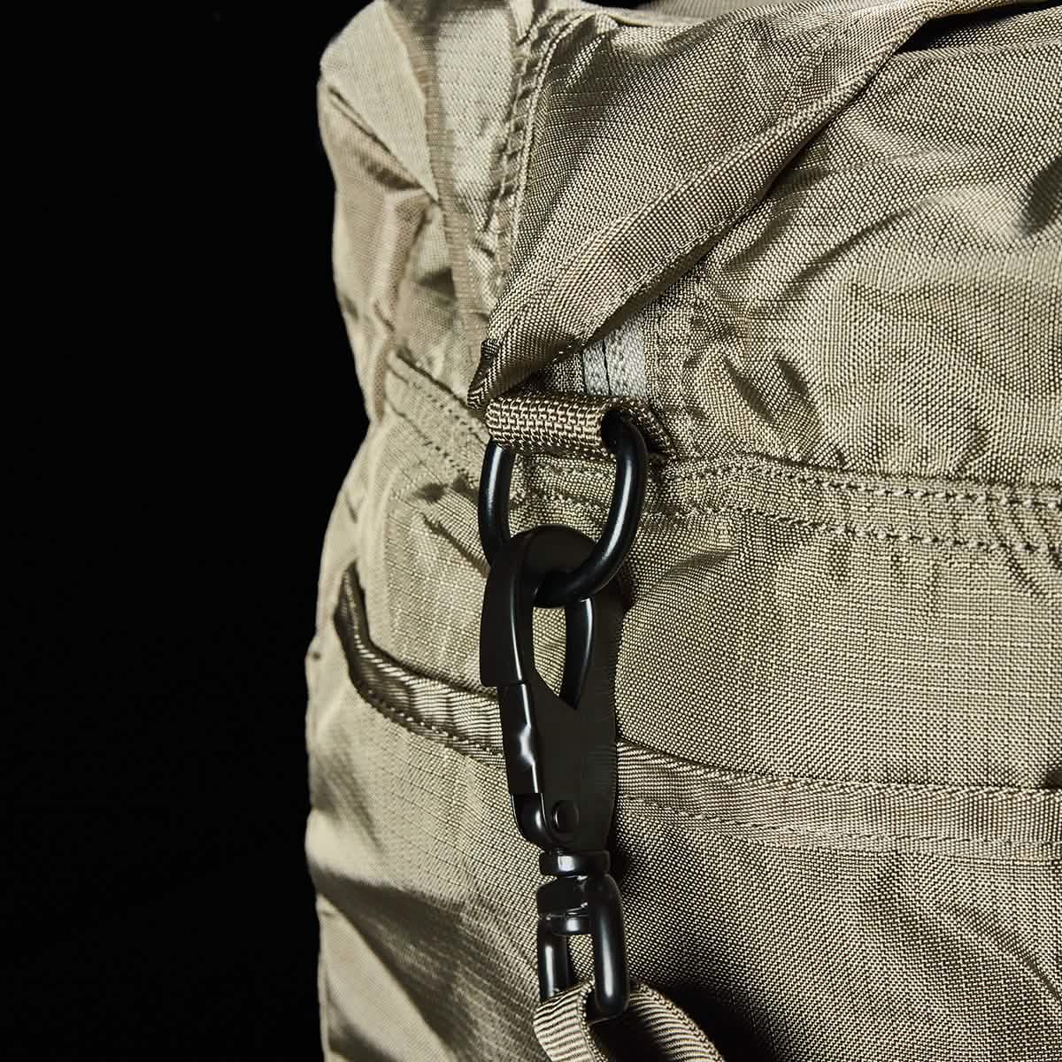 Close-up of a beige Kit Bag w/ Shoe Compartment - Ripstop ROBIC® by GORUCK, featuring a metal carabiner clip on its strap. The solid black background highlights the texture and stitching details of this versatile travel bag.