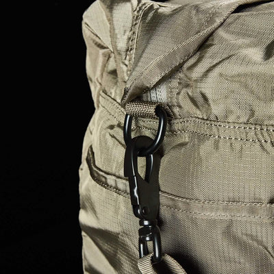Close-up of a beige Kit Bag w/ Shoe Compartment - Ripstop ROBIC® by GORUCK, featuring a metal carabiner clip on its strap. The solid black background highlights the texture and stitching details of this versatile travel bag.
