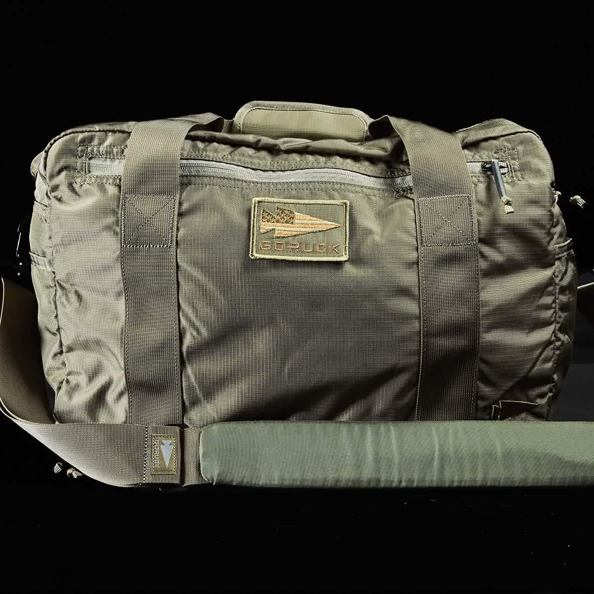 An olive green Kit Bag with a durable Special Forces Flight Bag design from GORUCK, featuring a long shoulder strap and two short handles. The bag includes a prominent patch displaying the GORUCK logo and brand name in the center.