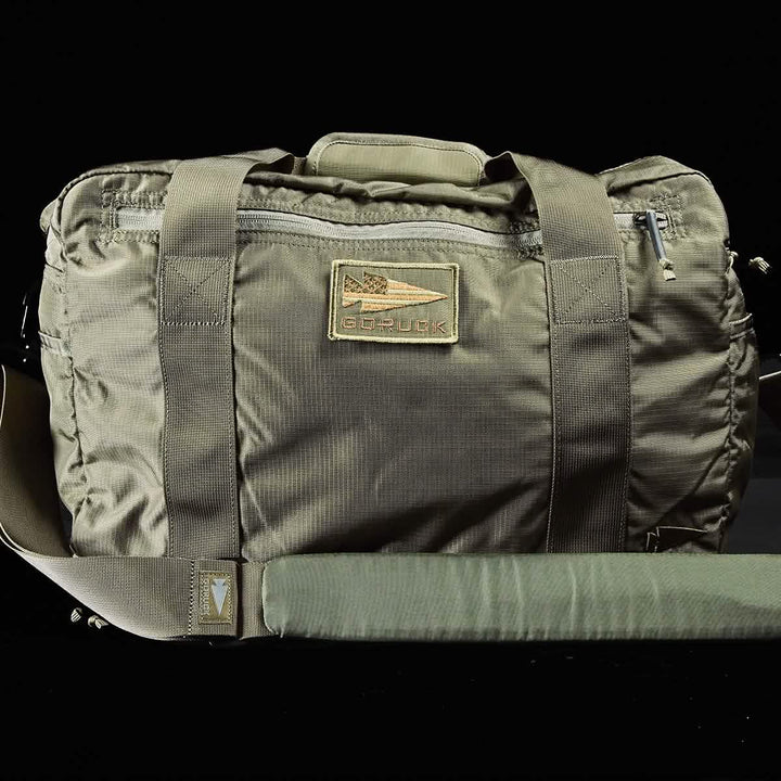 An olive green Kit Bag with a durable Special Forces Flight Bag design from GORUCK, featuring a long shoulder strap and two short handles. The bag includes a prominent patch displaying the GORUCK logo and brand name in the center.
