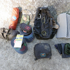 The GR MONSTER Bundle - PREORDER, featuring camping gear such as a GORUCK rucksack, tent, sleeping pad, map, bowls, gloves, and tarp, is arranged on the ground.