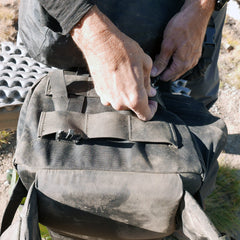Close-up of hands zipping a dusty black GR MONSTER Bundle - PREORDER rucksack outdoors on a sunny day.