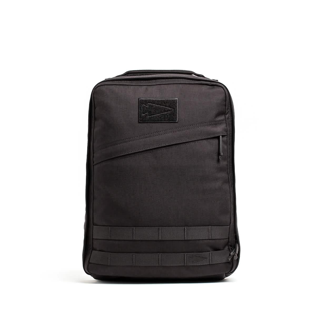 The GR0 - Cordura by GORUCK is a black rectangular compact backpack with a sleek, minimalist everyday carry design. It includes a front zippered pocket, a stitched arrow logo patch, and horizontal strap detailing at the bottom. The bag stands upright against a white background.