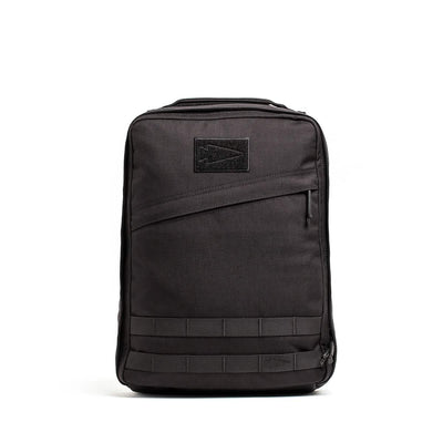 The GR0 - Cordura by GORUCK is a black rectangular compact backpack with a sleek, minimalist everyday carry design. It includes a front zippered pocket, a stitched arrow logo patch, and horizontal strap detailing at the bottom. The bag stands upright against a white background.