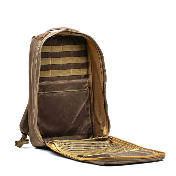 Open the GORUCK GR1 USA - Heritage in brown to reveal a main compartment and a mesh pocket on the inner flap. The interior is designed with multiple slots, accentuated by a moody lighting effect. Its rugged exterior is made from waxed duck canvas, featuring a Martexin Wax finish for added durability.