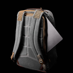 A GR1 USA - Heritage by GORUCK in gray, featuring padded straps and brown trim against a black background, is partially unzipped to showcase a laptop inside.