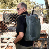 Man wearing GORUCK Heritage Slate 26L rucksack near fence, outdoor rugged setting