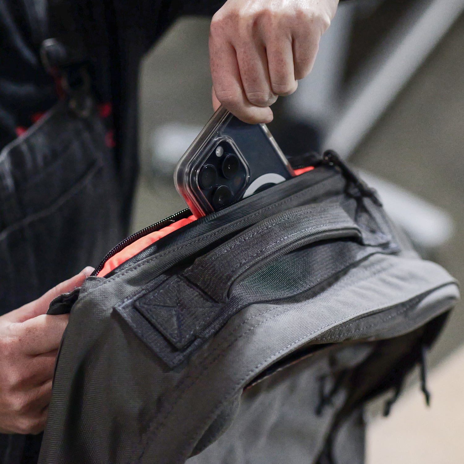A person puts a smartphone into the front pocket of a grey GR1 USA - Cordura, an everyday carry backpack known for Special Forces grade durability.
