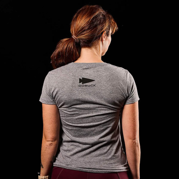 A person is seen from the back wearing a gray Women's CrossFit Tee - Tri-Blend by GORUCK against a black background. The shirt features a subtle "USA" print, adding a touch of patriotic flair to this elegant piece crafted from premium tri-blend fabric.