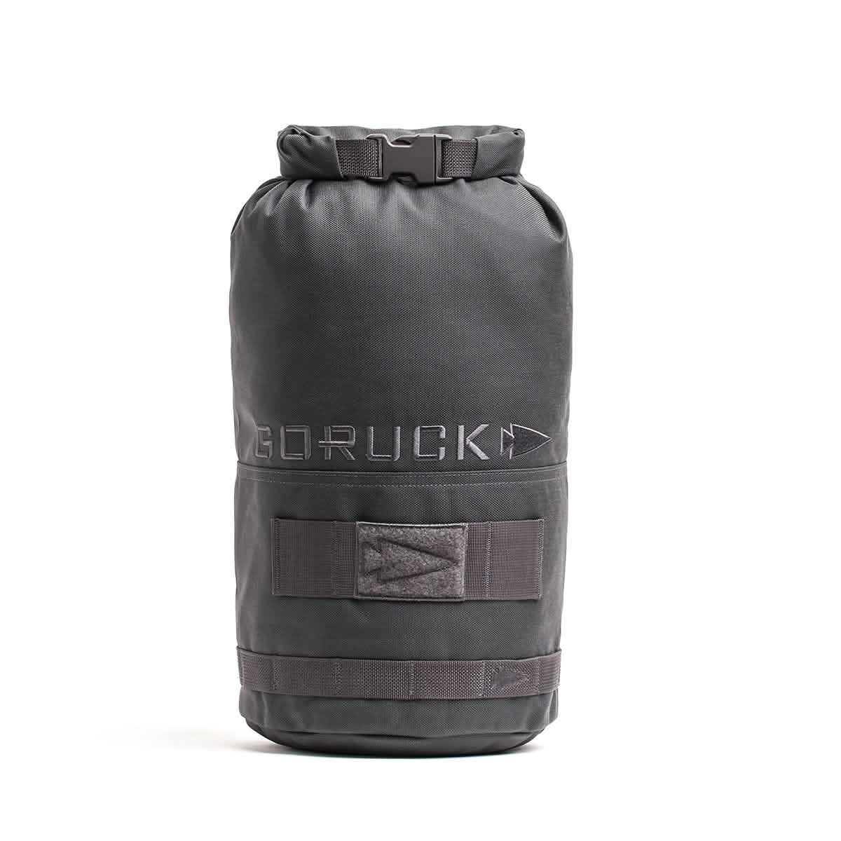 The Brick Bag (5-50 LBS) by GORUCK is a black cylindrical gym bag that stands upright and evokes the look of military gear. It boasts a roll-top closure and the GORUCK logo. Created for versatile training, it comes with adjustable straps and extra strap holders on the outside.