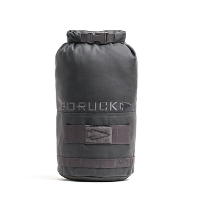 The Brick Bag (5-50 LBS) by GORUCK is a black cylindrical gym bag that stands upright and evokes the look of military gear. It boasts a roll-top closure and the GORUCK logo. Created for versatile training, it comes with adjustable straps and extra strap holders on the outside.