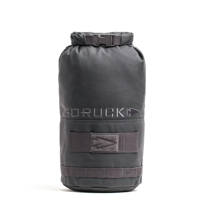 The Brick Bag (5-50 LBS) by GORUCK is a black cylindrical gym bag that stands upright and evokes the look of military gear. It boasts a roll-top closure and the GORUCK logo. Created for versatile training, it comes with adjustable straps and extra strap holders on the outside.