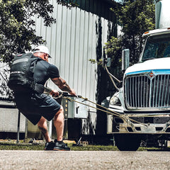 Man wearing GORUCK backpack performing heavy truck pull exercise outdoors