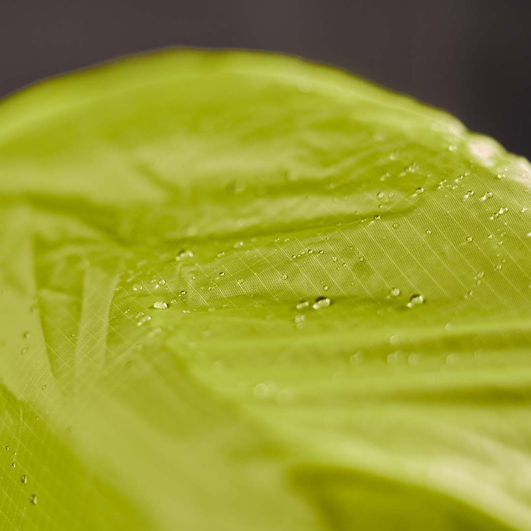 Close-up of water droplets on bright green, textured, waterproof fabric.