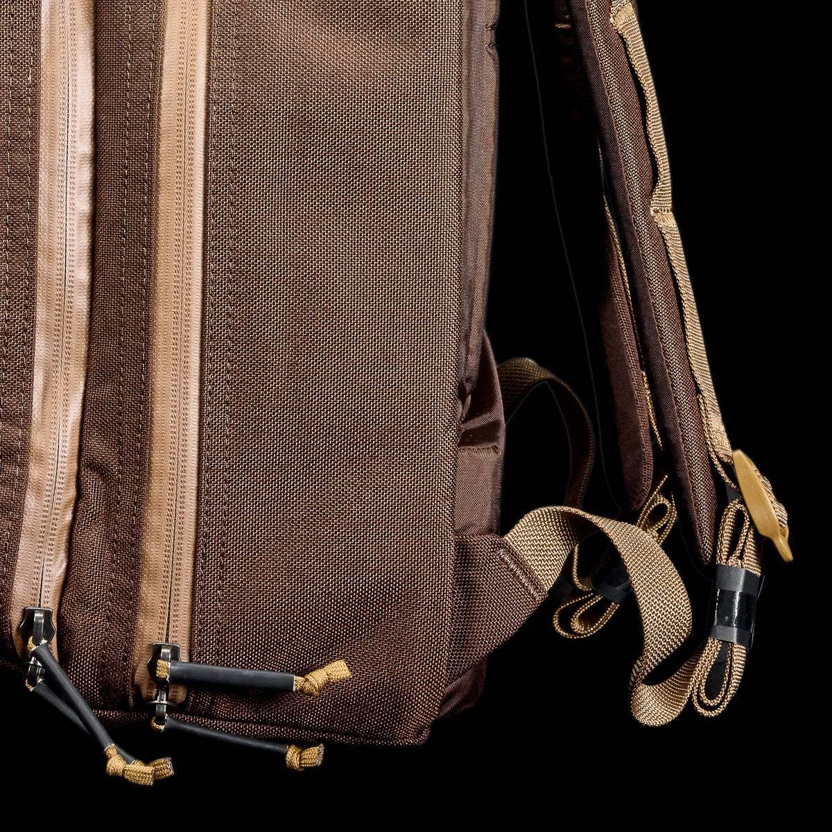 Close-up of a brown backpack with multiple zippers and straps, shown against a black background.