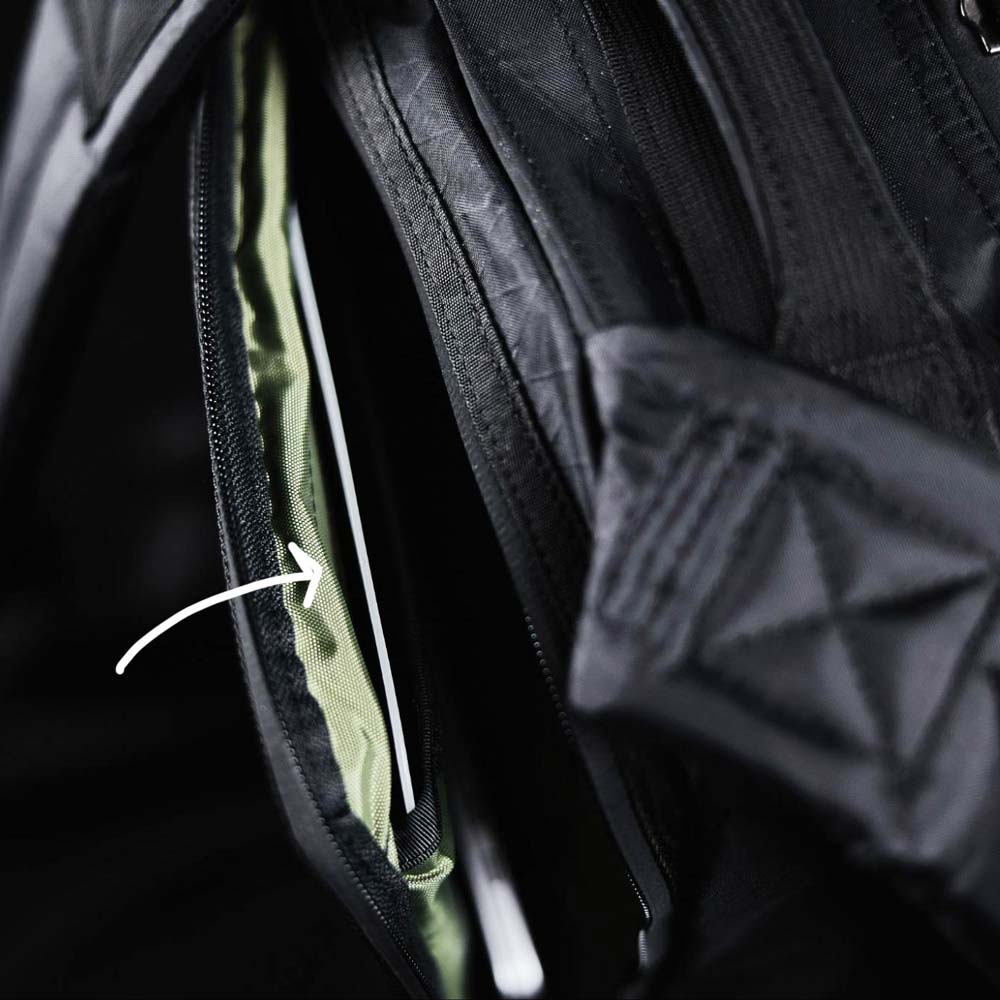 A close-up of a black backpack with a partially open zipper and an arrow pointing to an inside pocket.