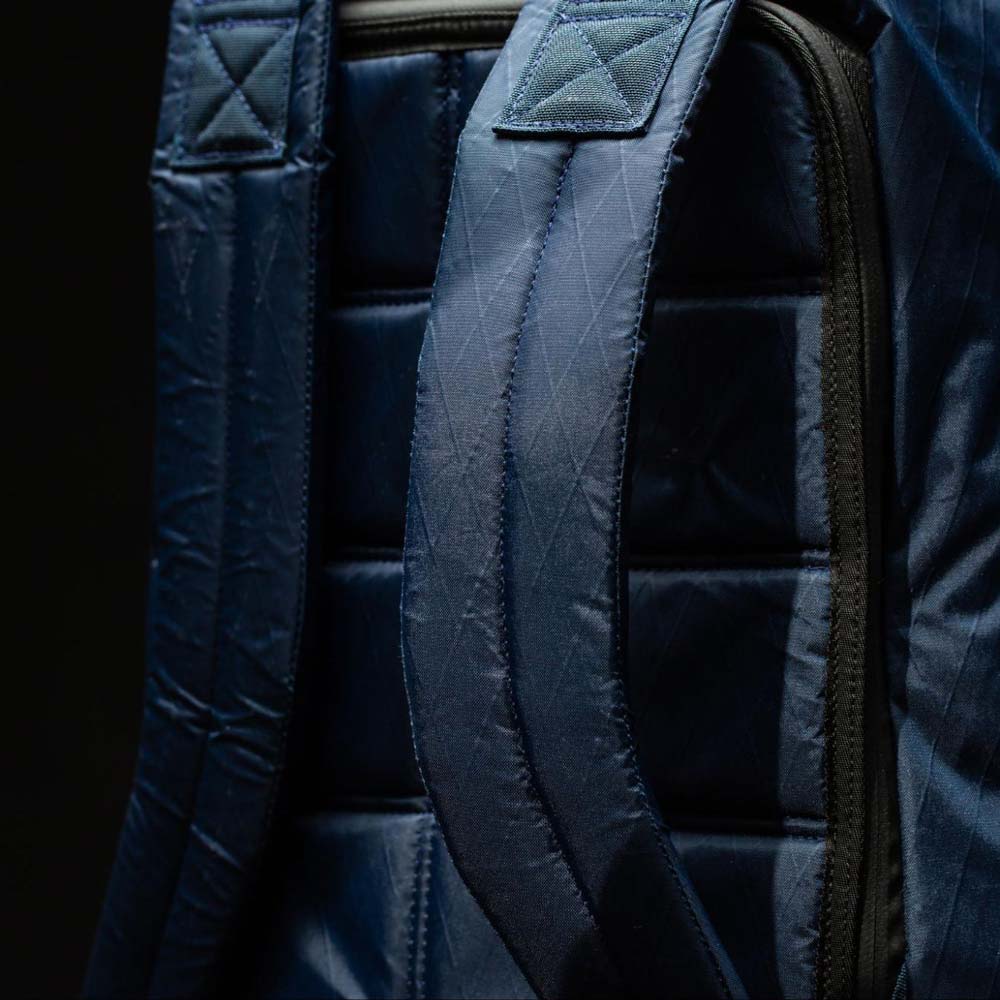 Close-up of dark blue quilted backpack straps with visible stitching details against a black background.
