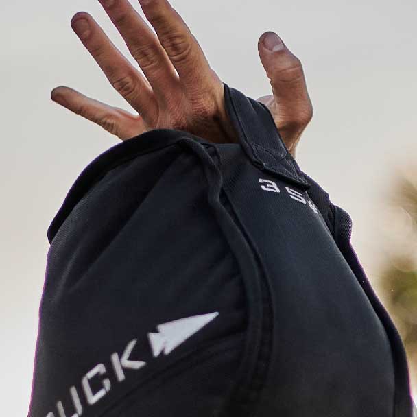 A hand gripping a black backpack strap with white text and an arrow logo visible on the bag.